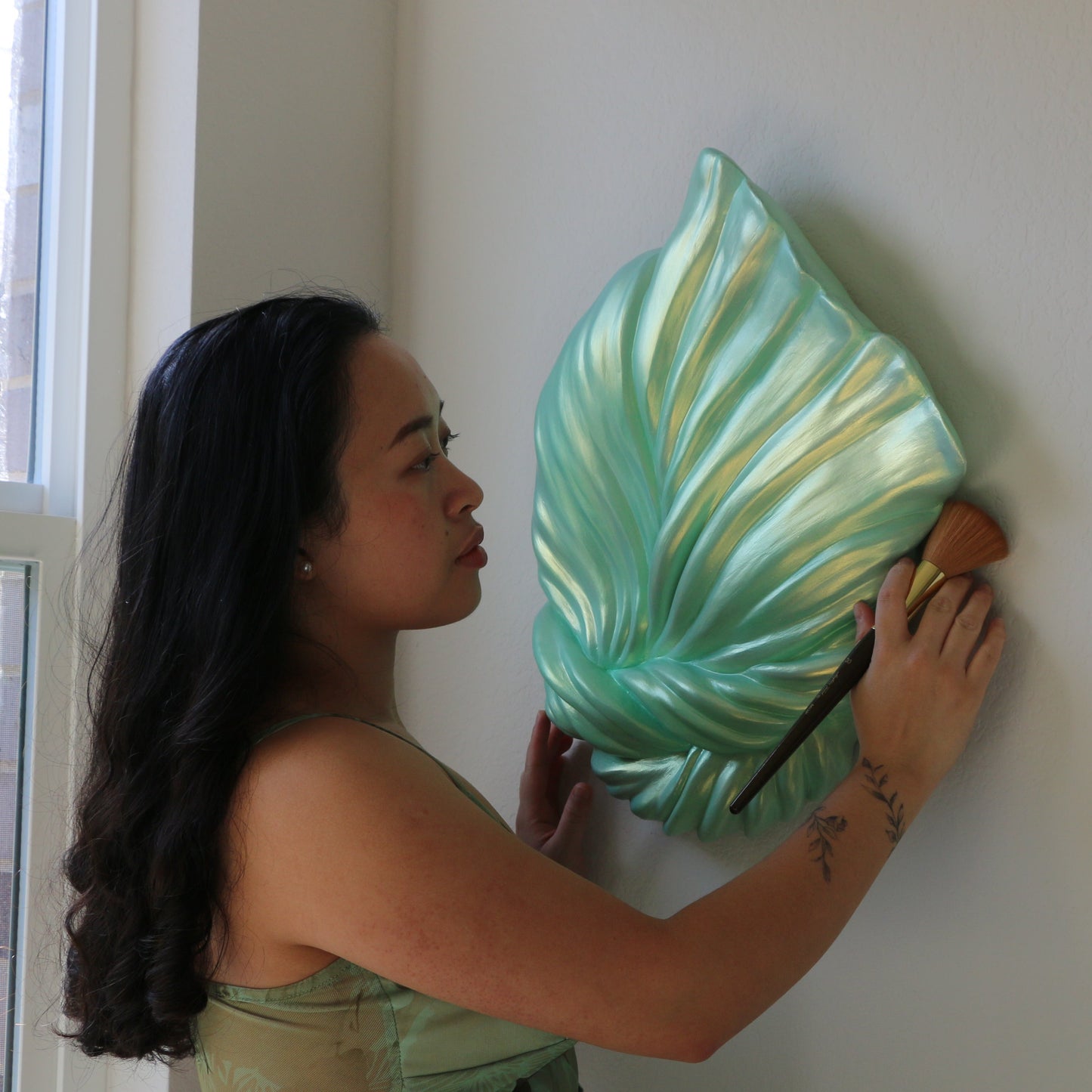 Artist hanging a decorative leaf wall piece on a white wall.