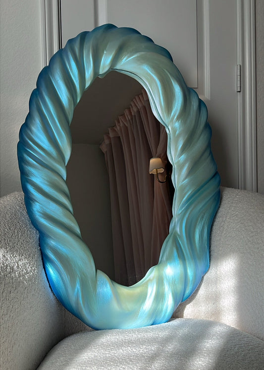 Decorative mirror with a blue, wavy frame on a white surface.