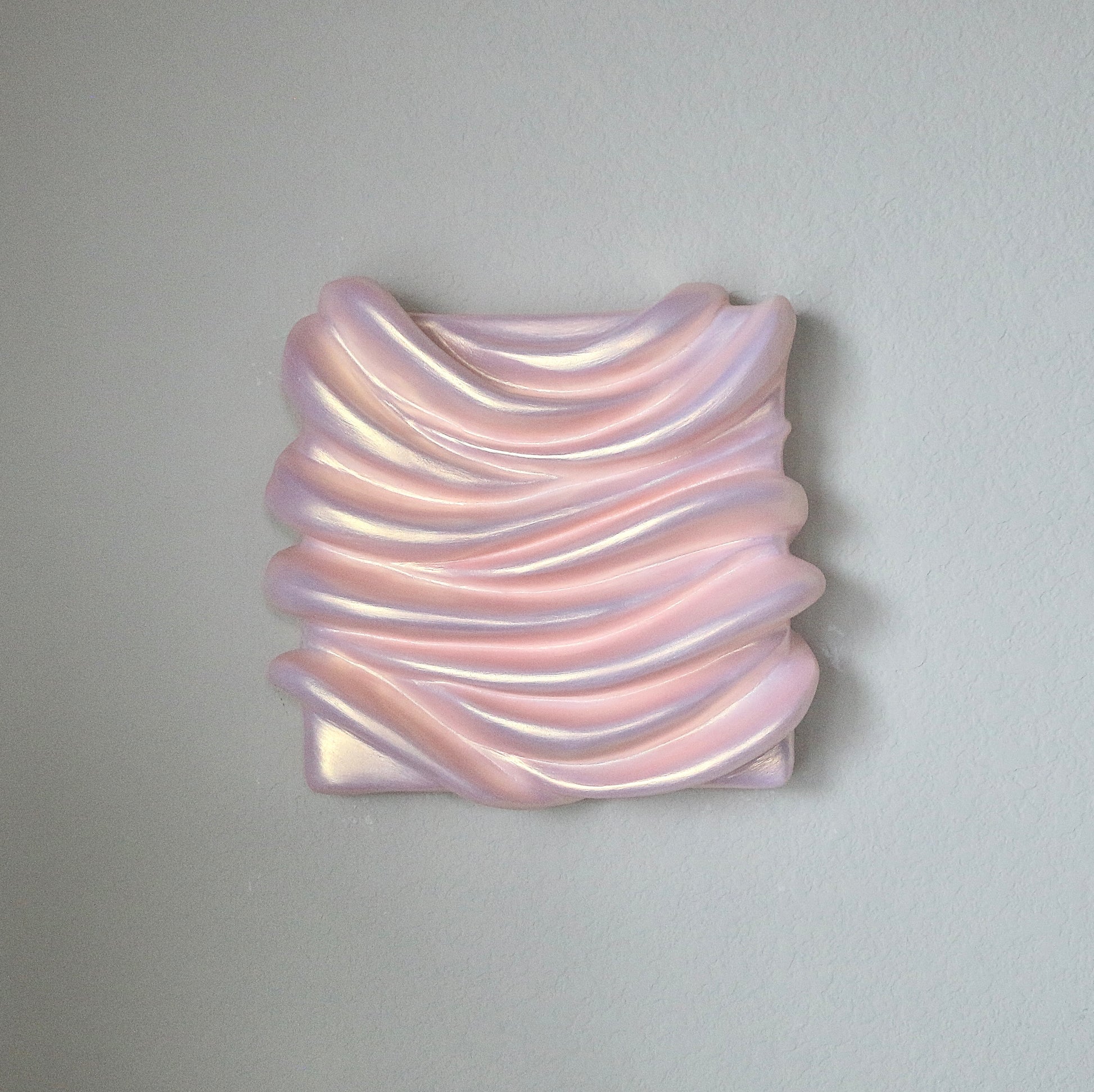 A sculpture artwork represented as a abstract, amorphous form with a smooth, possibly metallic surface in an pinkish hue, mounted on a wall.