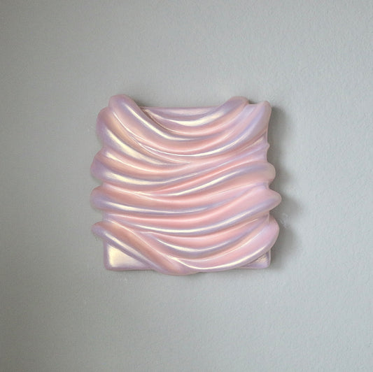 A sculpture artwork represented as a abstract, amorphous form with a smooth, possibly metallic surface in an pinkish hue, mounted on a wall.