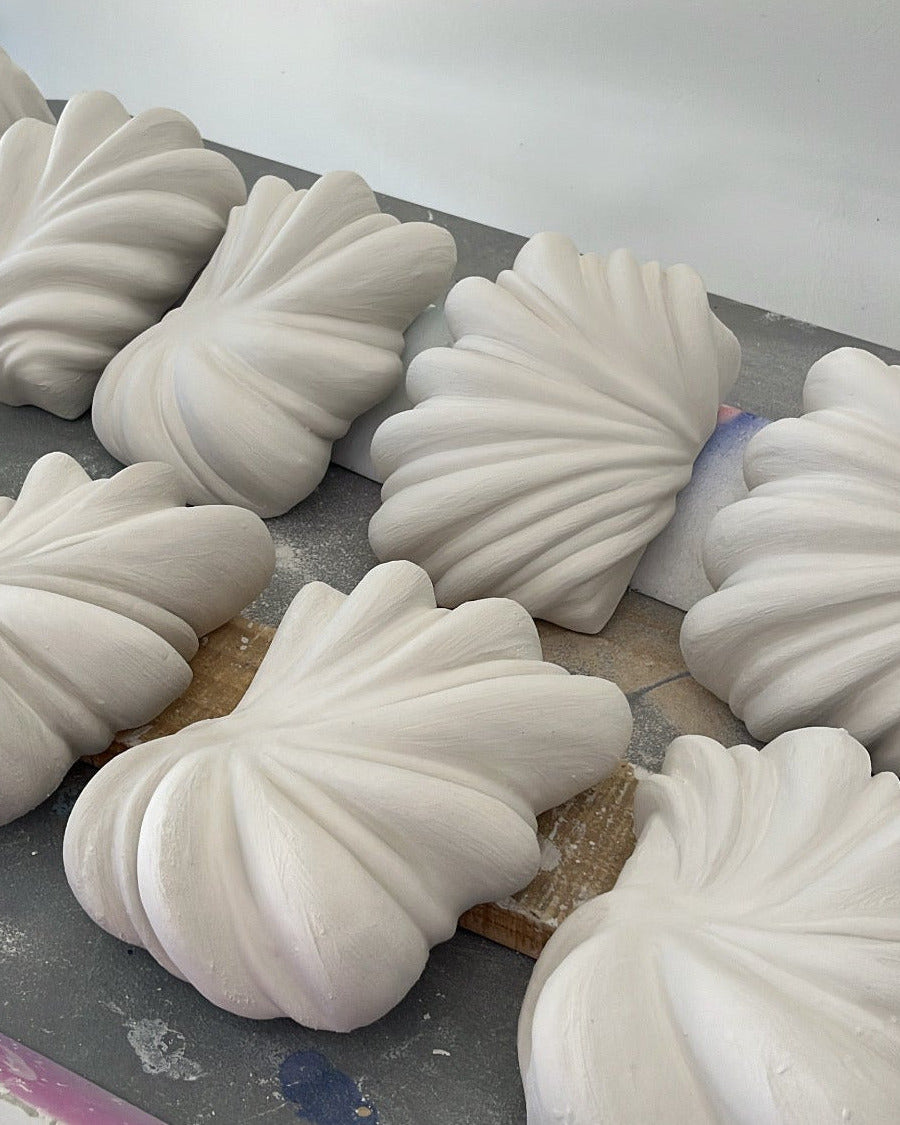 Several white ribbed decorative art or sculptural pieces arranged on a gray work surface against a plain light background.