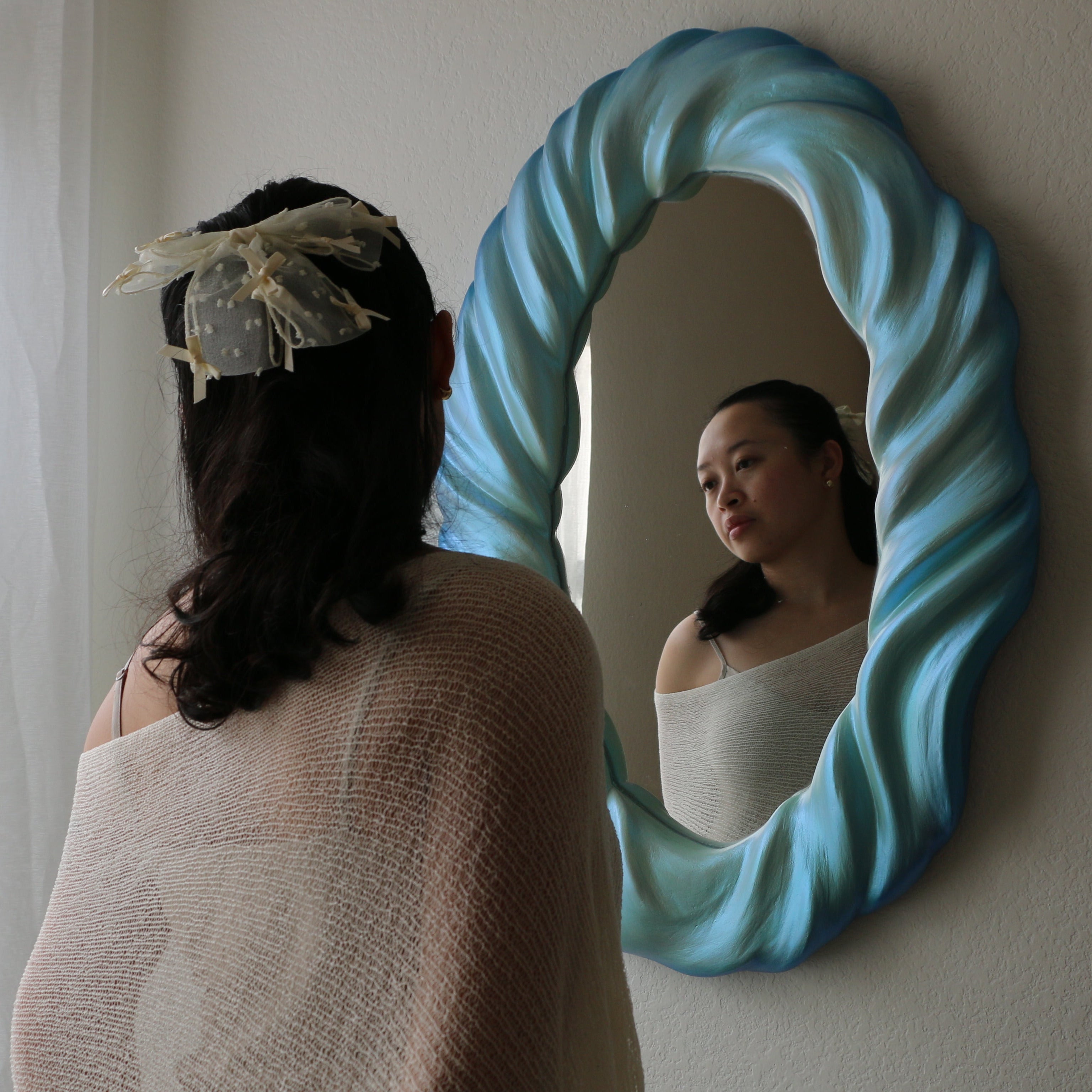 Woman looking at herself in a blue wavy mirror.