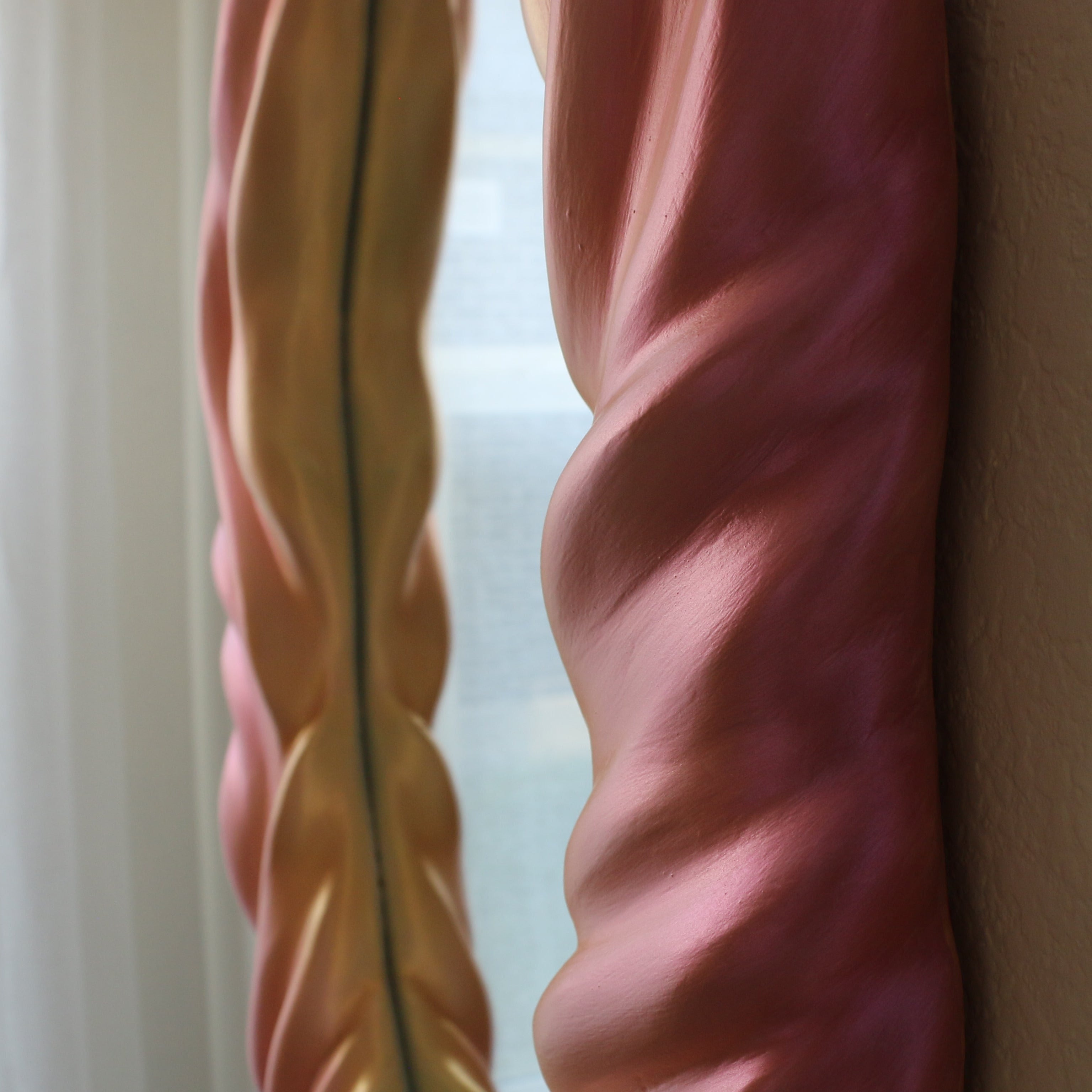 Decorative pink and gold spiral framed mirror art leaning against a wall.